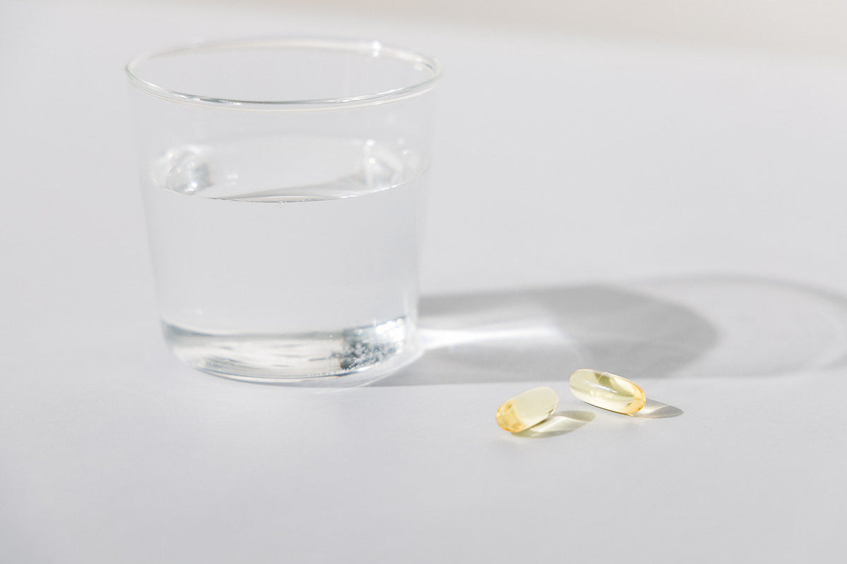 Fish Oil Softgels placed on a counter next to a glass of water