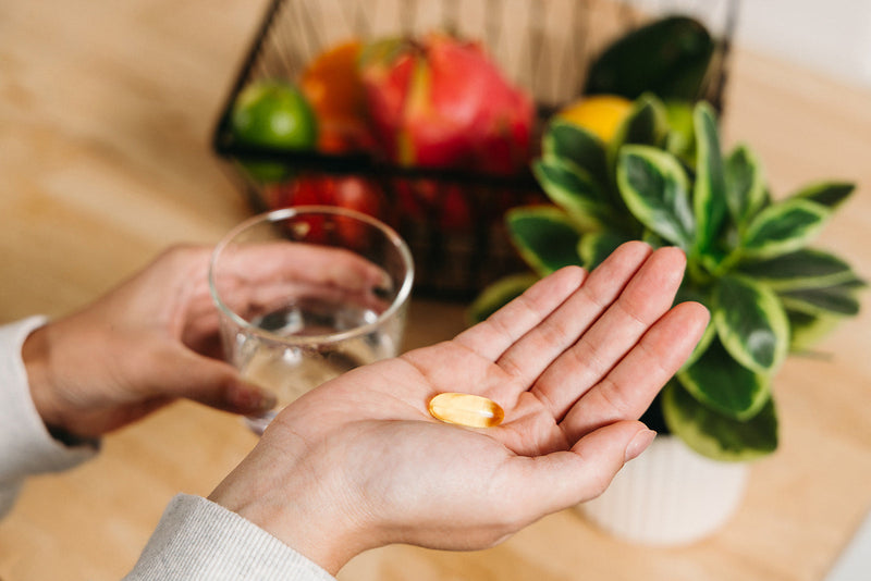 A person taking their Wiley's Finest Peak EPA Omega-3 Supplement with a glass of water.