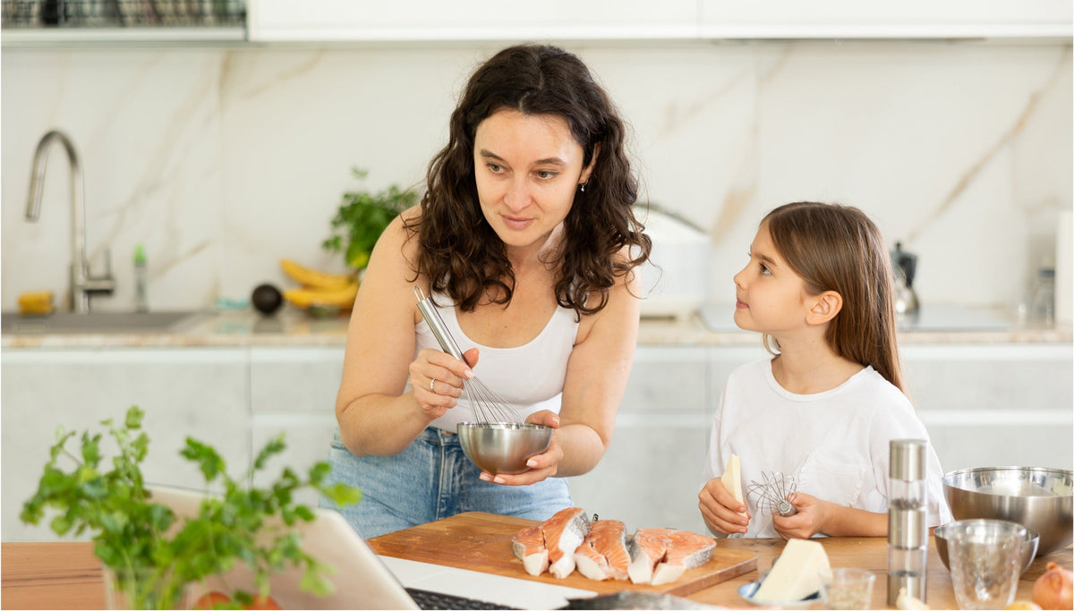 Mother and daughter prepare a meal together in a bright kitchen, with fresh salmon on a cutting board.